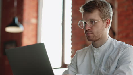 freelancer-is-working-with-laptop-in-cafe-closeup-portrait-of-concentrated-face-of-attractive-man-with-glasses
